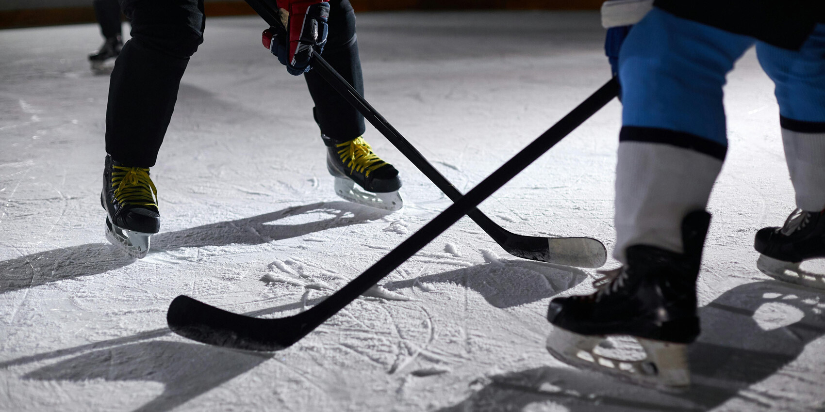 Close-up of two hockey players facing off on an ice rink, their skates and sticks poised, capturing the intensity of Hockey Fighting and What it Means to Be A Man as they battle for the puck.