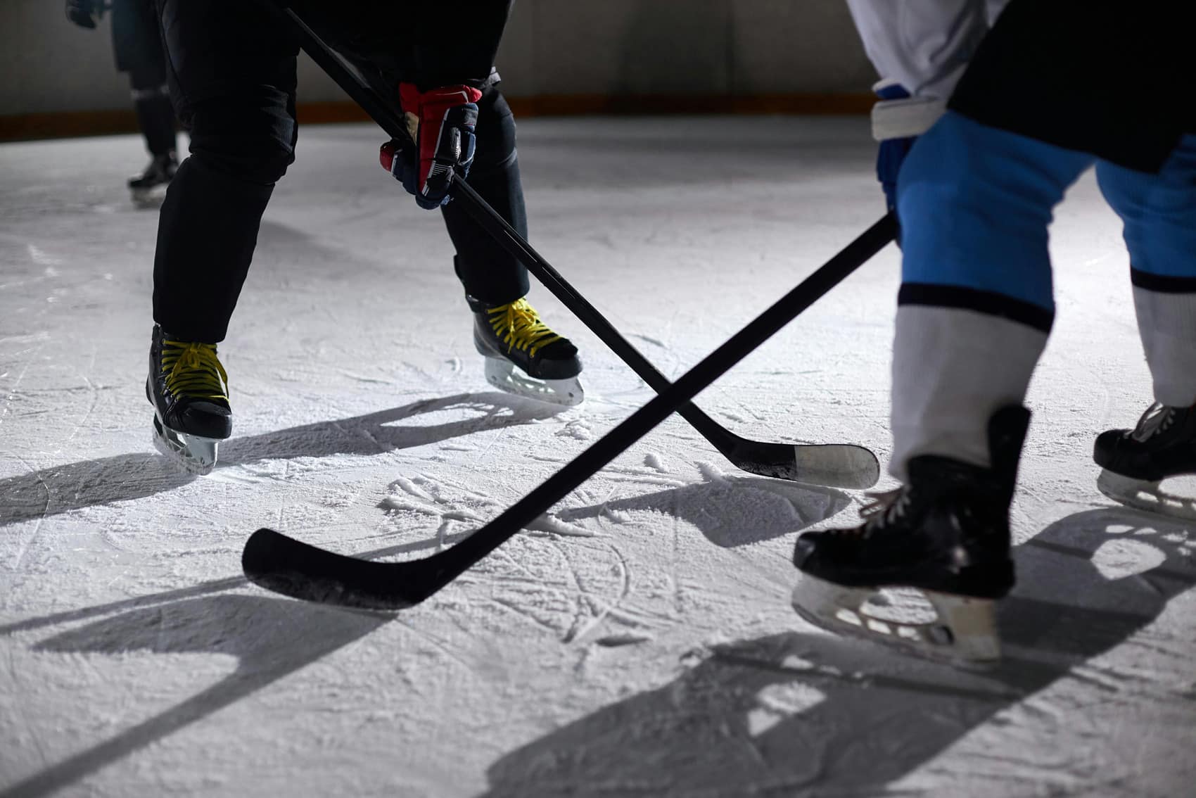 Close-up of two hockey players facing off on an ice rink, their skates and sticks poised, capturing the intensity of Hockey Fighting and What it Means to Be A Man as they battle for the puck.