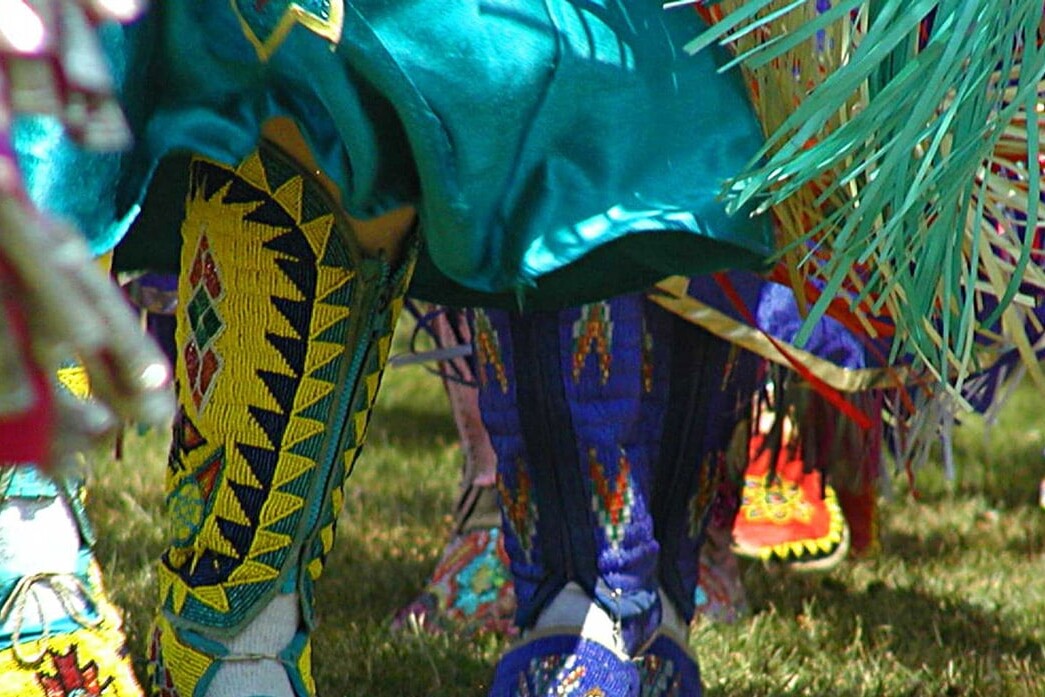 Close-up of dancers’ feet and legs in colorful, beaded moccasins and fringed regalia on grass at a powwow—showcasing what success might look like for young Aboriginals embracing tradition and cultural pride.
