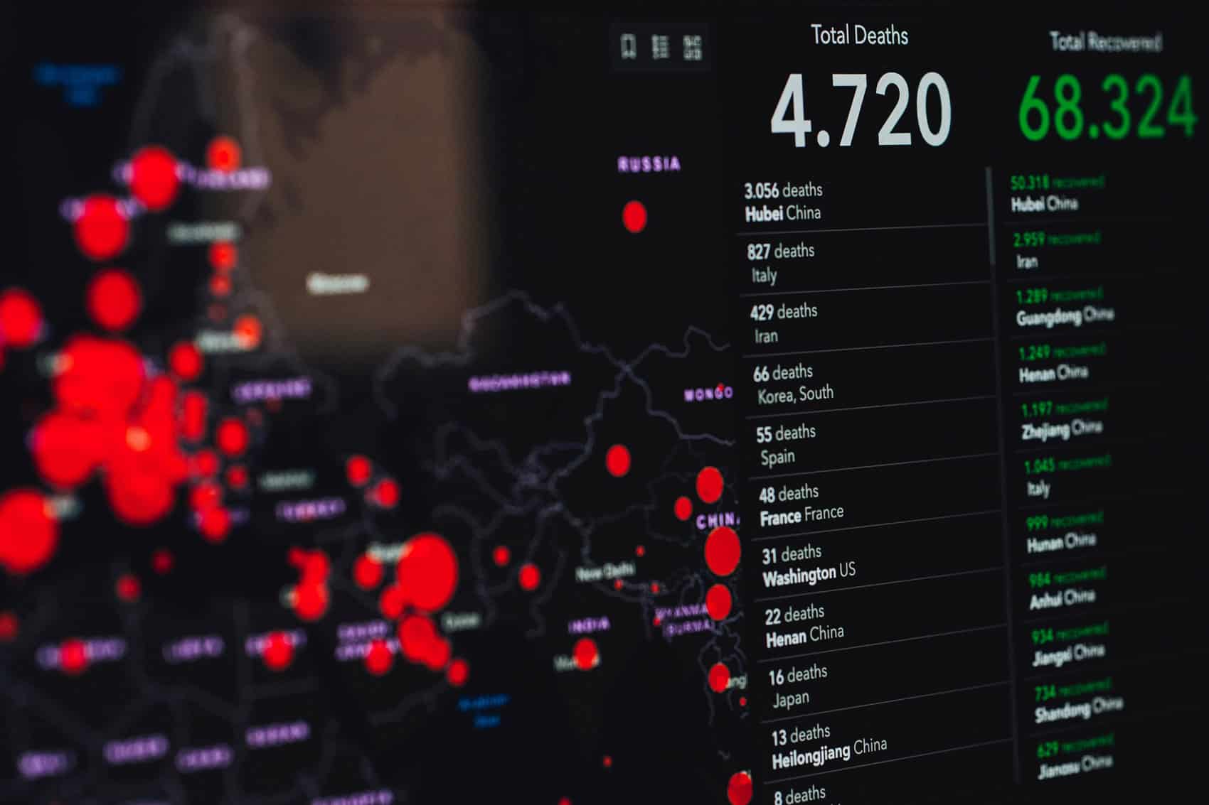 A digital dashboard shows a world map with large red circles for outbreak locations and a stats panel listing 4,720 deaths and 68,324 recovered—putting the 