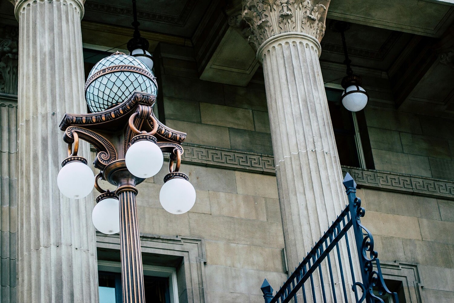 A vintage street lamp with globe lights stands in front of a stone building featuring tall, ornate columns—a scene reminiscent of classic debates like, 