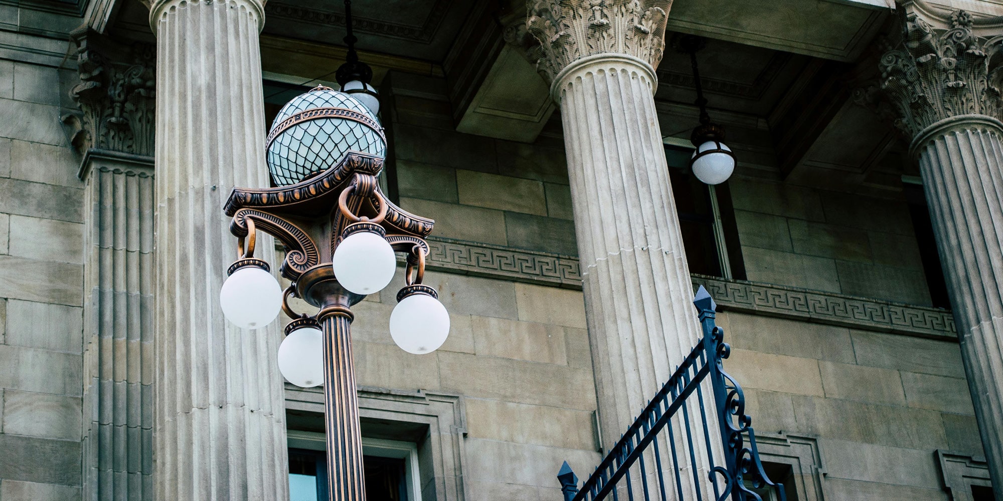 A vintage street lamp with globe lights stands in front of a stone building featuring tall, ornate columns—a scene reminiscent of classic debates like, 