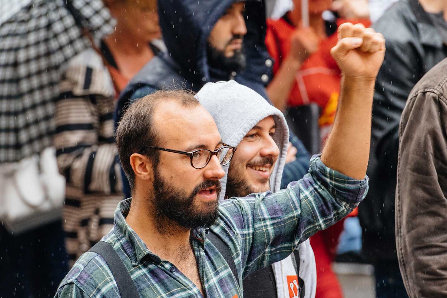 A group of people in casual clothing march in the rain. One man in glasses and a plaid shirt raises his fist, reflecting a sense of unity and purpose—reminding us that democracies are stronger than you may think.