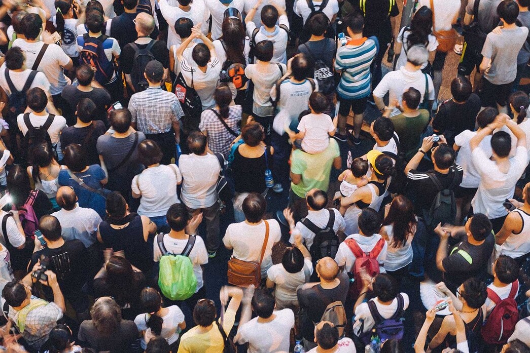 A large crowd of people seen from above, standing close together—many with backpacks and casual clothing—creates a dense scene, reminiscent of the diversity in sanctuary cities: why it's harder for Trumpism to take root in Canadian cities.