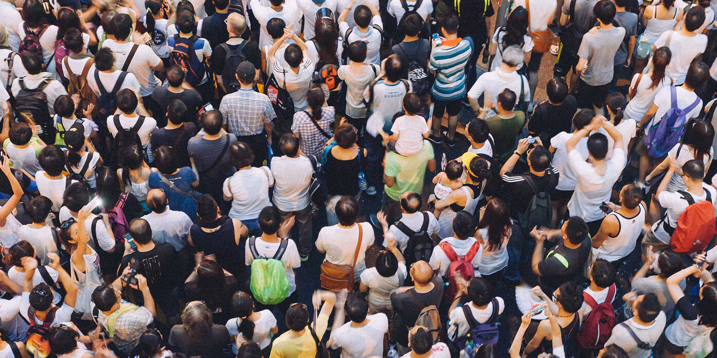 A large crowd of people seen from above, standing close together—many with backpacks and casual clothing—creates a dense scene, reminiscent of the diversity in sanctuary cities: why it's harder for Trumpism to take root in Canadian cities.