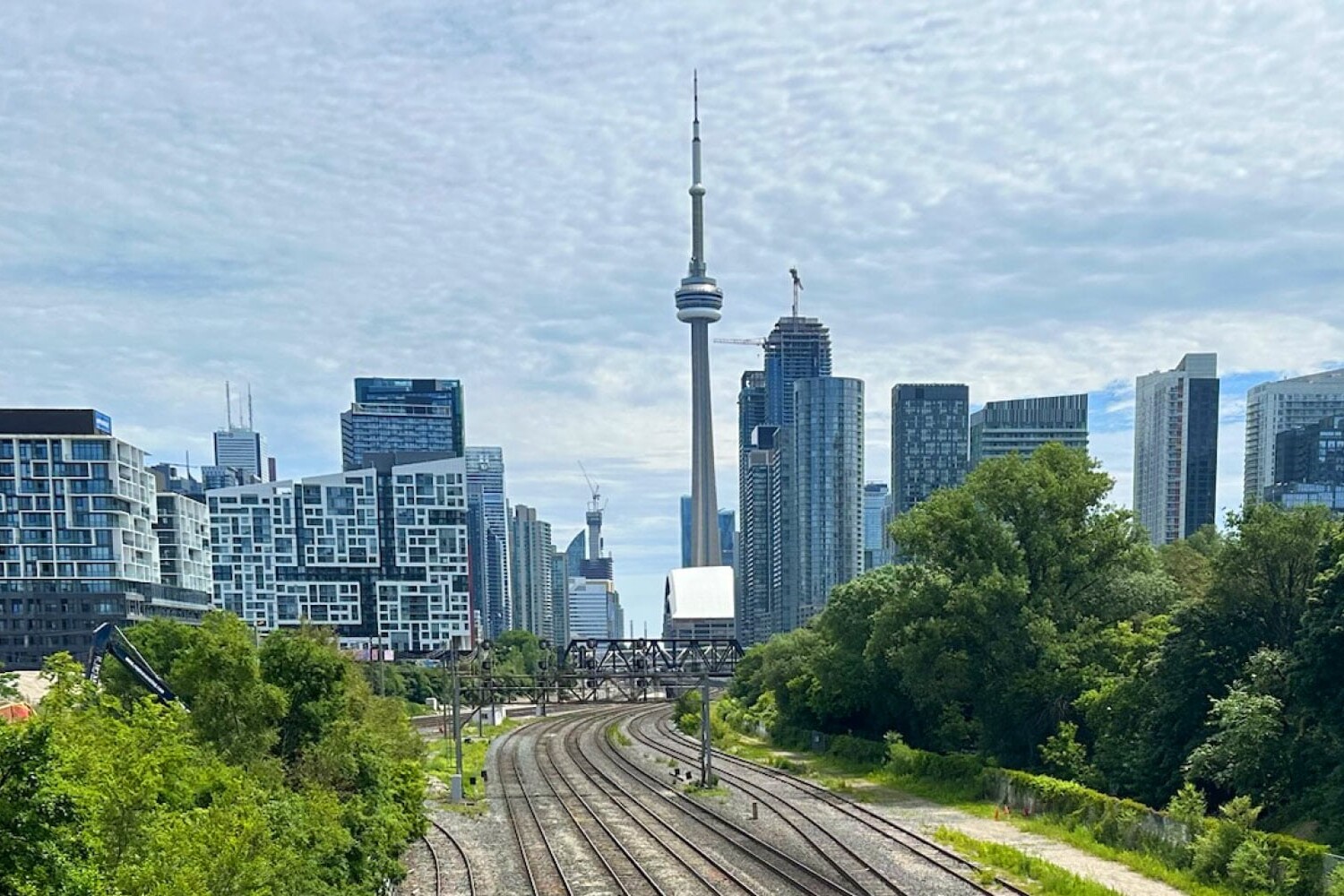 Downtown Toronto skyline with the CN Tower in the center, surrounded by modern high-rise buildings and railway tracks curving through green trees—an inspiring scene when considering three ways that Toronto could become more autonomous from Ontario.