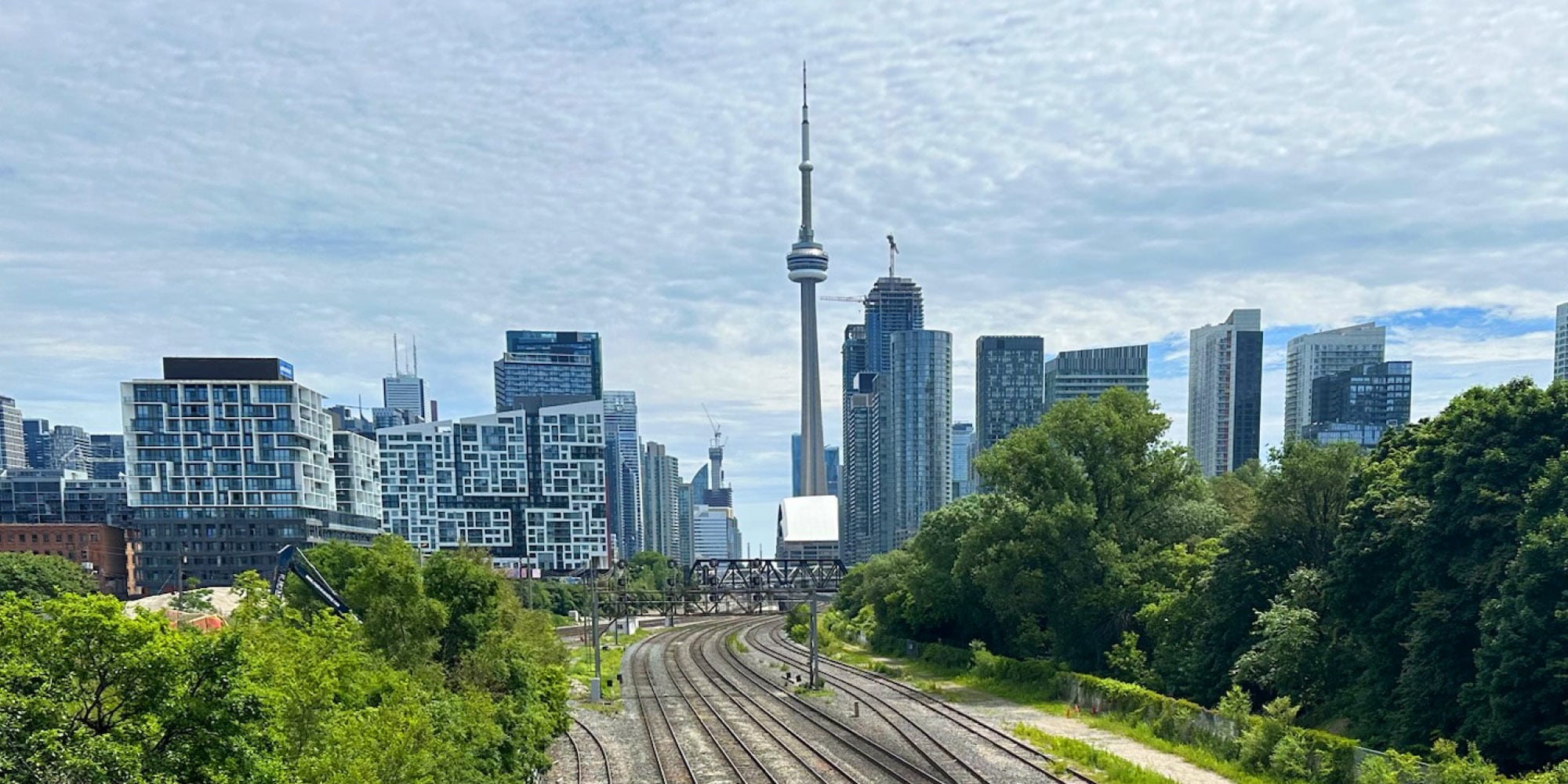 Downtown Toronto skyline with the CN Tower in the center, surrounded by modern high-rise buildings and railway tracks curving through green trees—an inspiring scene when considering three ways that Toronto could become more autonomous from Ontario.