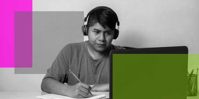 A young person wearing headphones sits at a desk, looking at a laptop screen and taking notes with a pencil—an image reflecting 