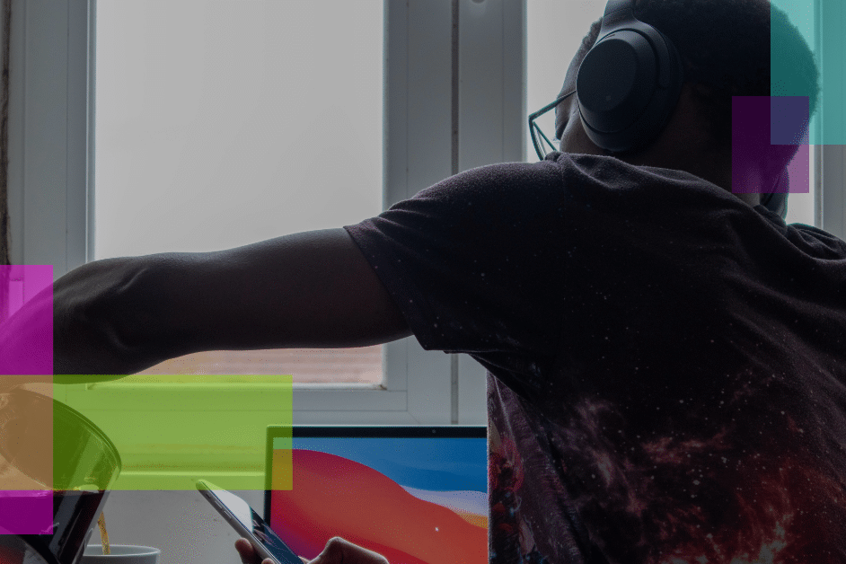 Illustrating the shift to remote work, a person wearing headphones pours a drink while using a tablet at a desk in front of a window. An open laptop and colorful translucent rectangles complete the modern work-from-home scene.