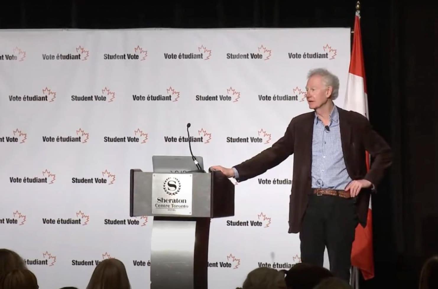 A man stands at a podium labeled Sheraton Centre Toronto, speaking at an event with a Student Vote and Vote &eacute;tudiant backdrop. Embarking on a Social Values Journey Down Memory Lane, a Canadian flag is visible to the right.