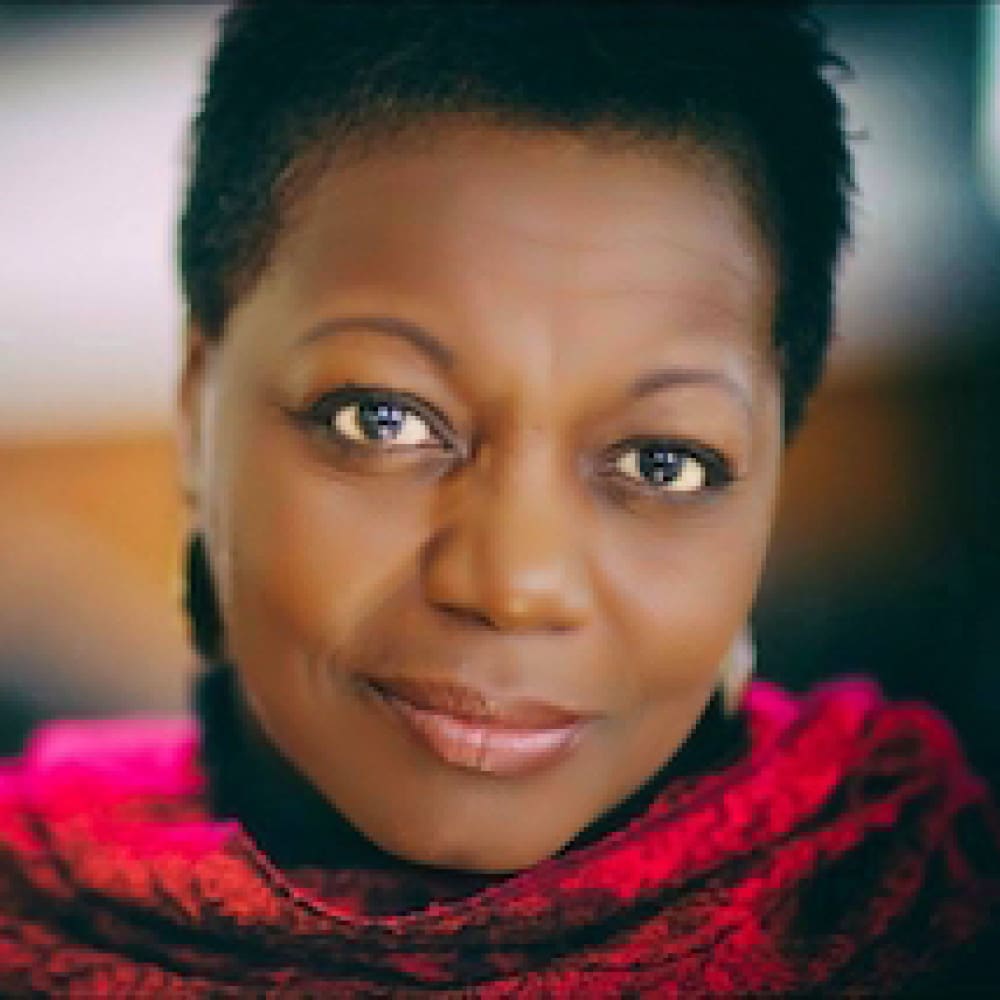 A woman with short hair smiles softly, wearing a vibrant red textured scarf. The background is blurred, drawing attention to her expressive eyes and warm expression—captured in the distinctive style of Andrew Griffith.
