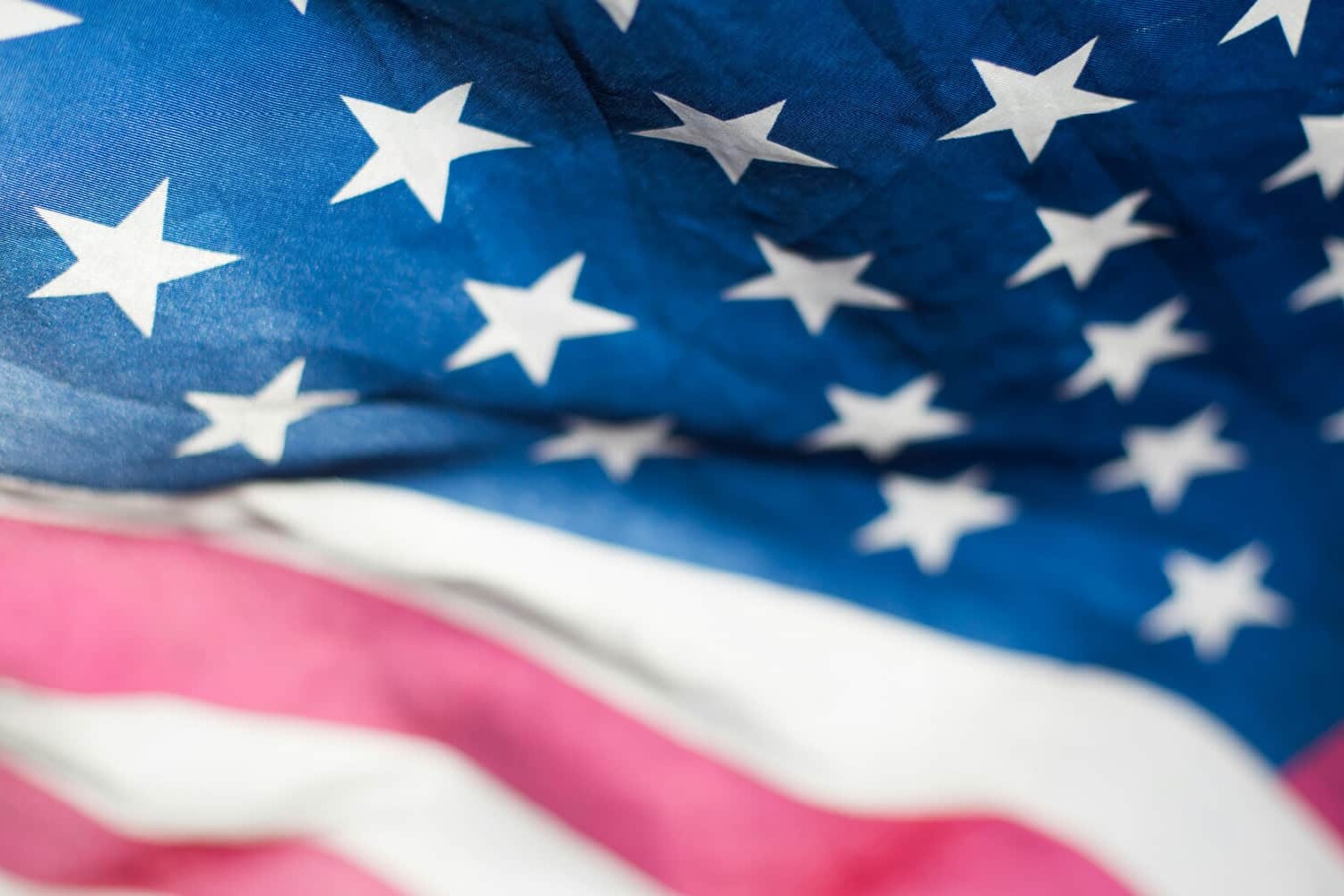 A close-up of the United States flag, showing white stars on a blue field and red and white stripes. The fabric appears slightly wrinkled, suggesting movement—much like Canadian public opinion on free trade.