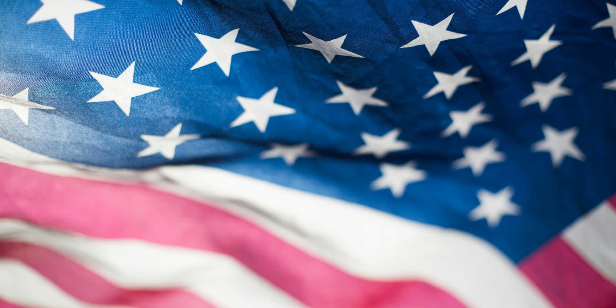 A close-up of the United States flag, showing white stars on a blue field and red and white stripes. The fabric appears slightly wrinkled, suggesting movement—much like Canadian public opinion on free trade.