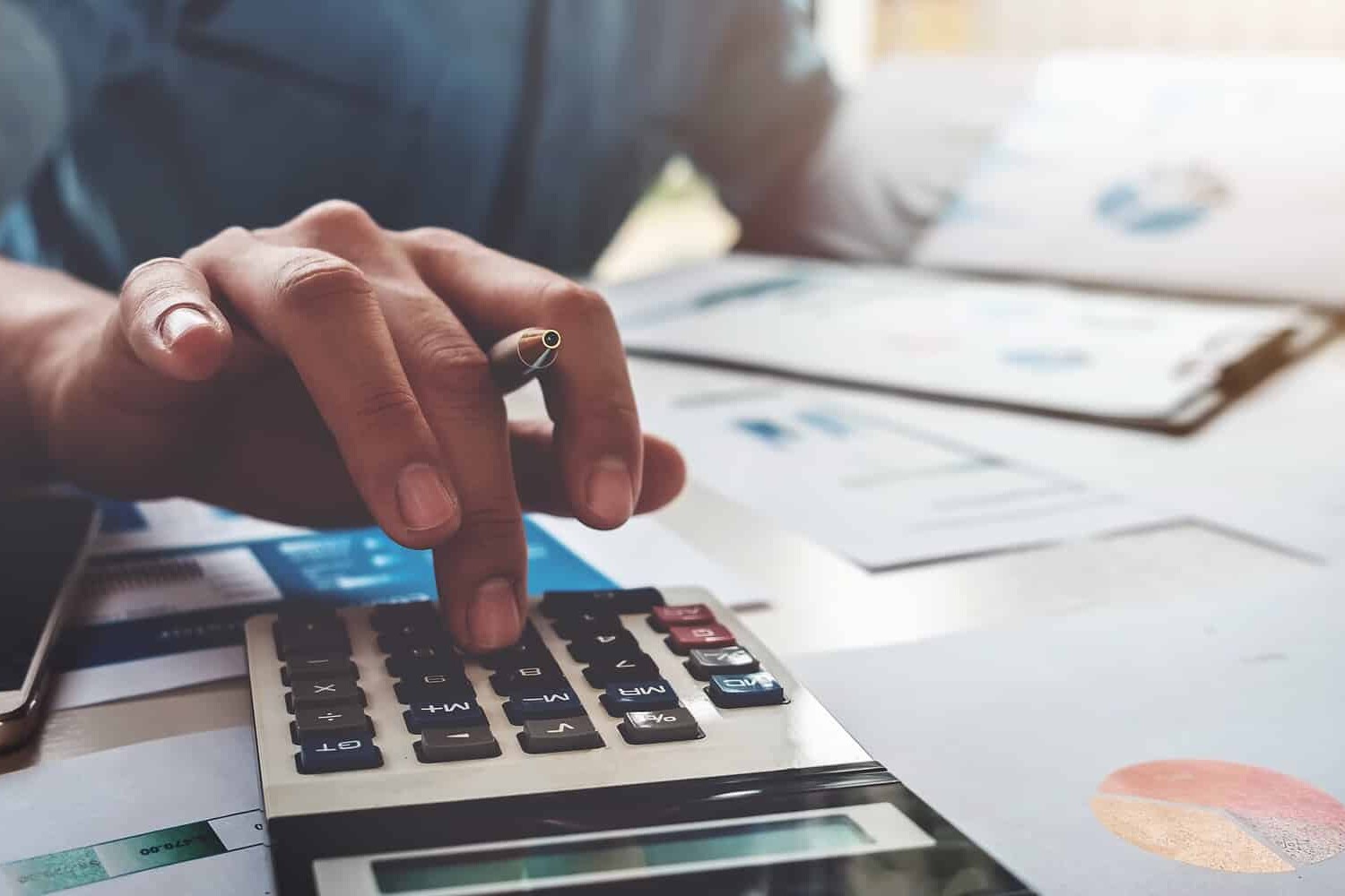 A person uses a calculator on a desk covered with financial documents and charts, holding a pen in one hand and appearing to review data or make calculations—reminding us that Canada can’t afford to be complacent about skills training.