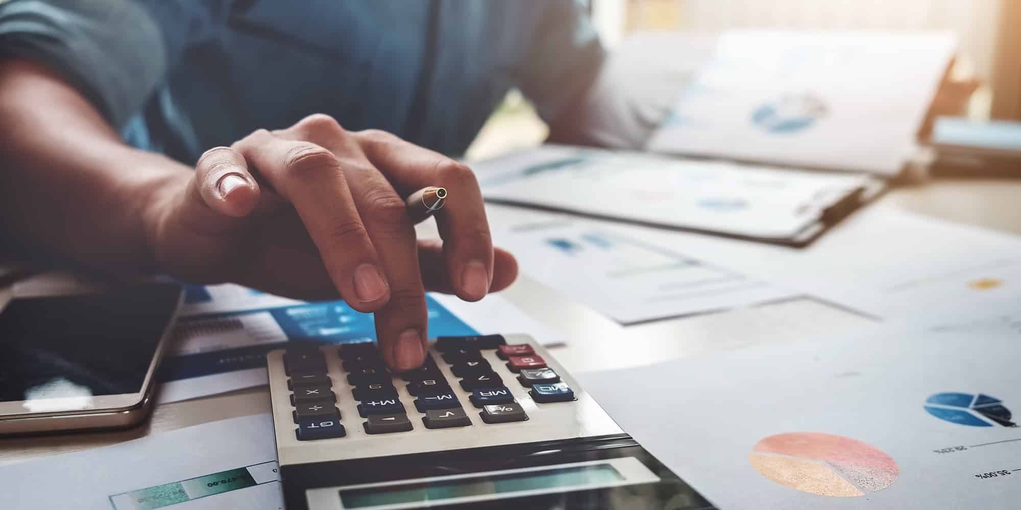 A person uses a calculator on a desk covered with financial documents and charts, holding a pen in one hand and appearing to review data or make calculations—reminding us that Canada can’t afford to be complacent about skills training.