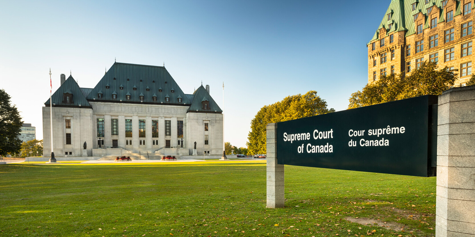 The Supreme Court of Canada building stands behind a large bilingual sign reading Supreme Court of Canada / Cour suprême du Canada, symbolizing its pivotal role in upholding the Charter of Rights, with trees and grass in the foreground under a clear sky.