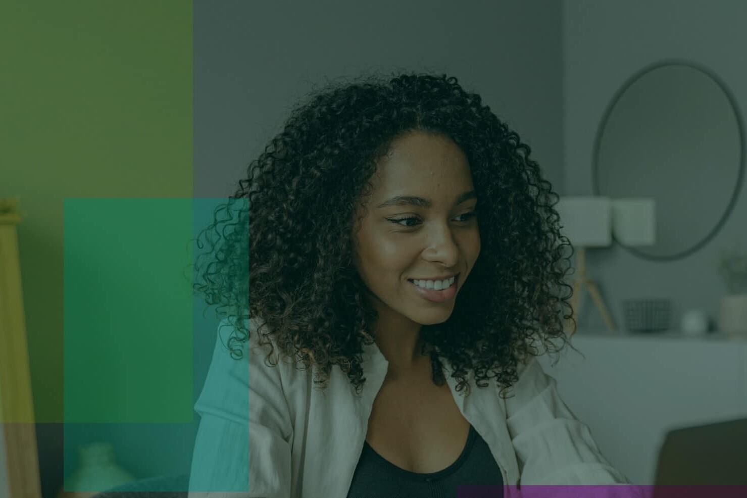 A woman with curly hair smiles while looking at something offscreen. She is indoors, with modern decor and soft lighting—capturing a moment that reflects how working from home is affecting the workplace. Translucent colored squares overlay part of the image.