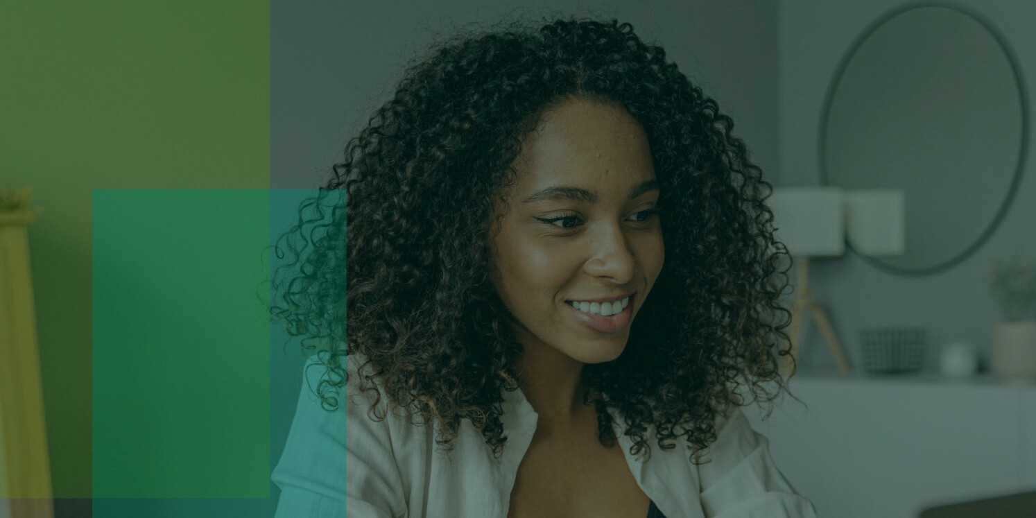 A woman with curly hair smiles while looking at something offscreen. She is indoors, with modern decor and soft lighting—capturing a moment that reflects how working from home is affecting the workplace. Translucent colored squares overlay part of the image.
