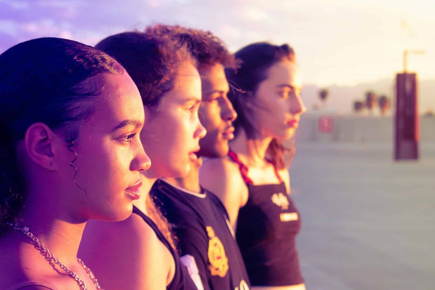 Four young people stand side by side outdoors at sunset, looking ahead with serious expressions—a reminder that Canadians need to keep talking about racism as the warm sunlight casts a golden glow across their faces and the open, blurred background.