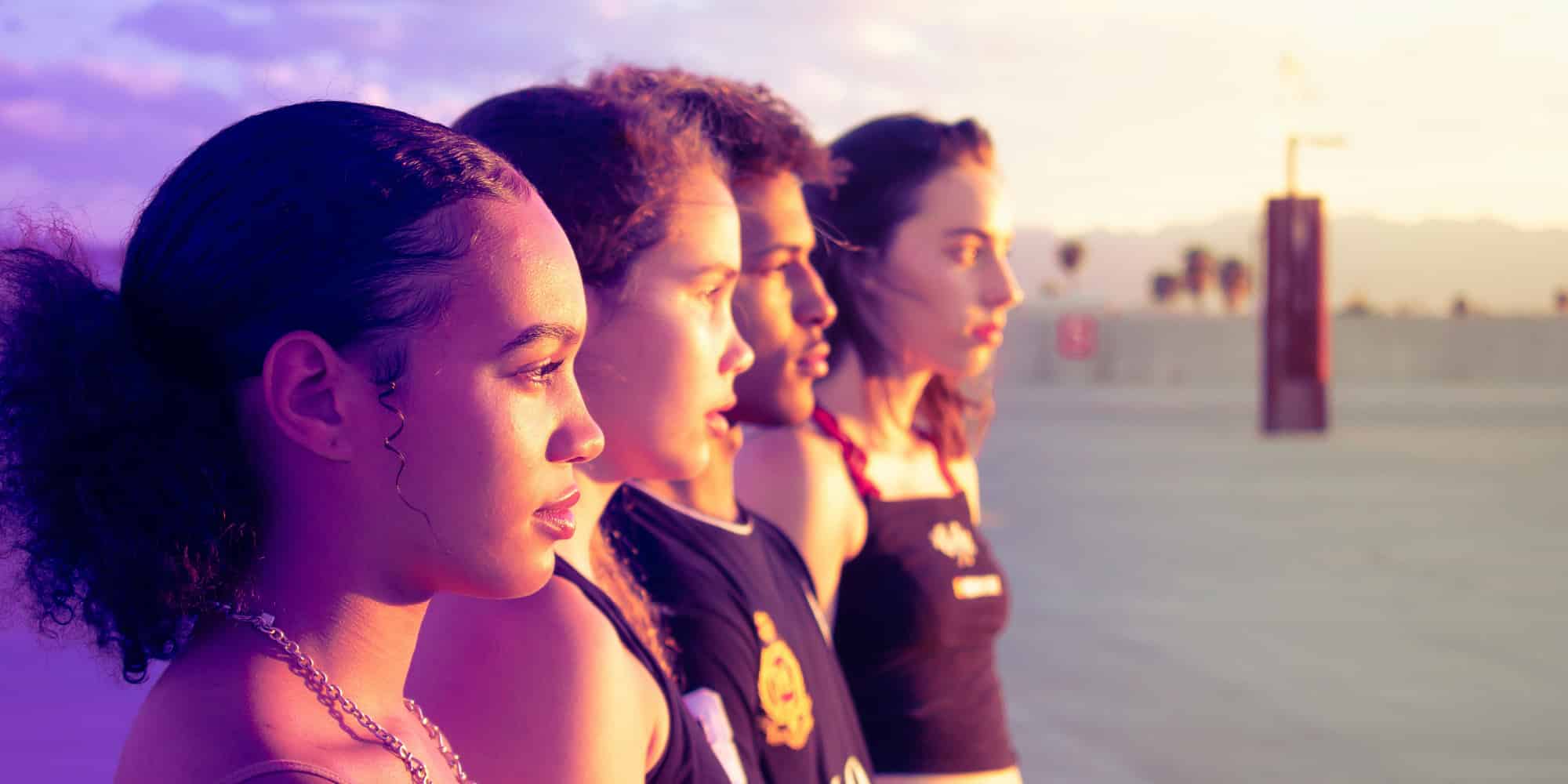Four young people stand side by side outdoors at sunset, looking ahead with serious expressions—a reminder that Canadians need to keep talking about racism as the warm sunlight casts a golden glow across their faces and the open, blurred background.