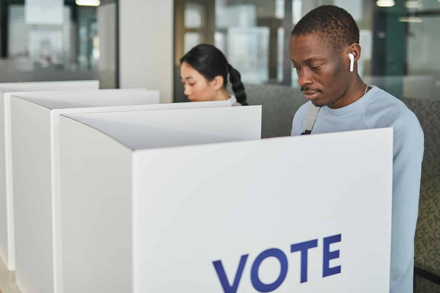 Two people stand at separate voting booths casting their votes, VOTE printed in large blue letters. In this modern polling station, having an election that changes nothing is not such a bad outcome after all.