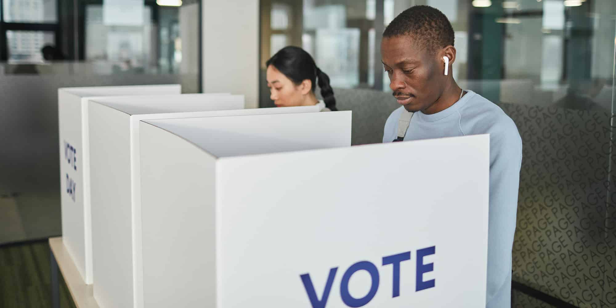 Two people stand at separate voting booths casting their votes, VOTE printed in large blue letters. In this modern polling station, having an election that changes nothing is not such a bad outcome after all.