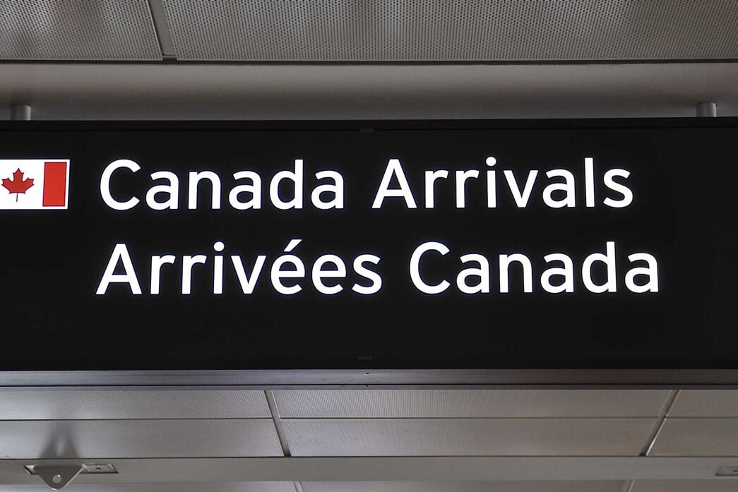 A bilingual airport sign with a Canadian flag points to Canada Arrivals in English and Arrivées Canada in French, subtly reminding travelers that private sponsorship is much more than a feel-good project—it's part of Canada's welcoming spirit.
