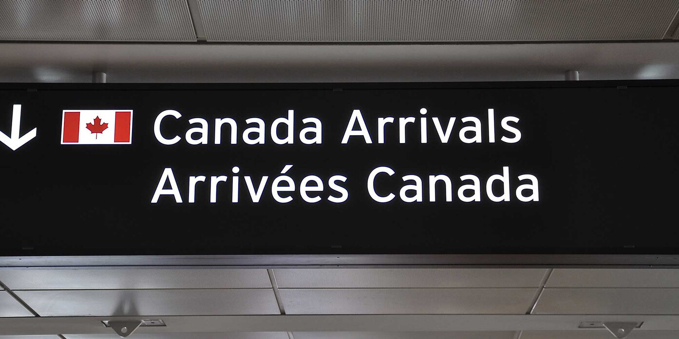 A bilingual airport sign with a Canadian flag points to Canada Arrivals in English and Arrivées Canada in French, subtly reminding travelers that private sponsorship is much more than a feel-good project—it's part of Canada's welcoming spirit.