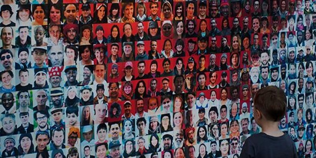 A young boy stands before a wall filled with hundreds of faces in a grid, showcasing the diversity of ages, genders, and ethnicities—reflecting intercultural relations and adaptation in Canada amid contact and discrimination.
