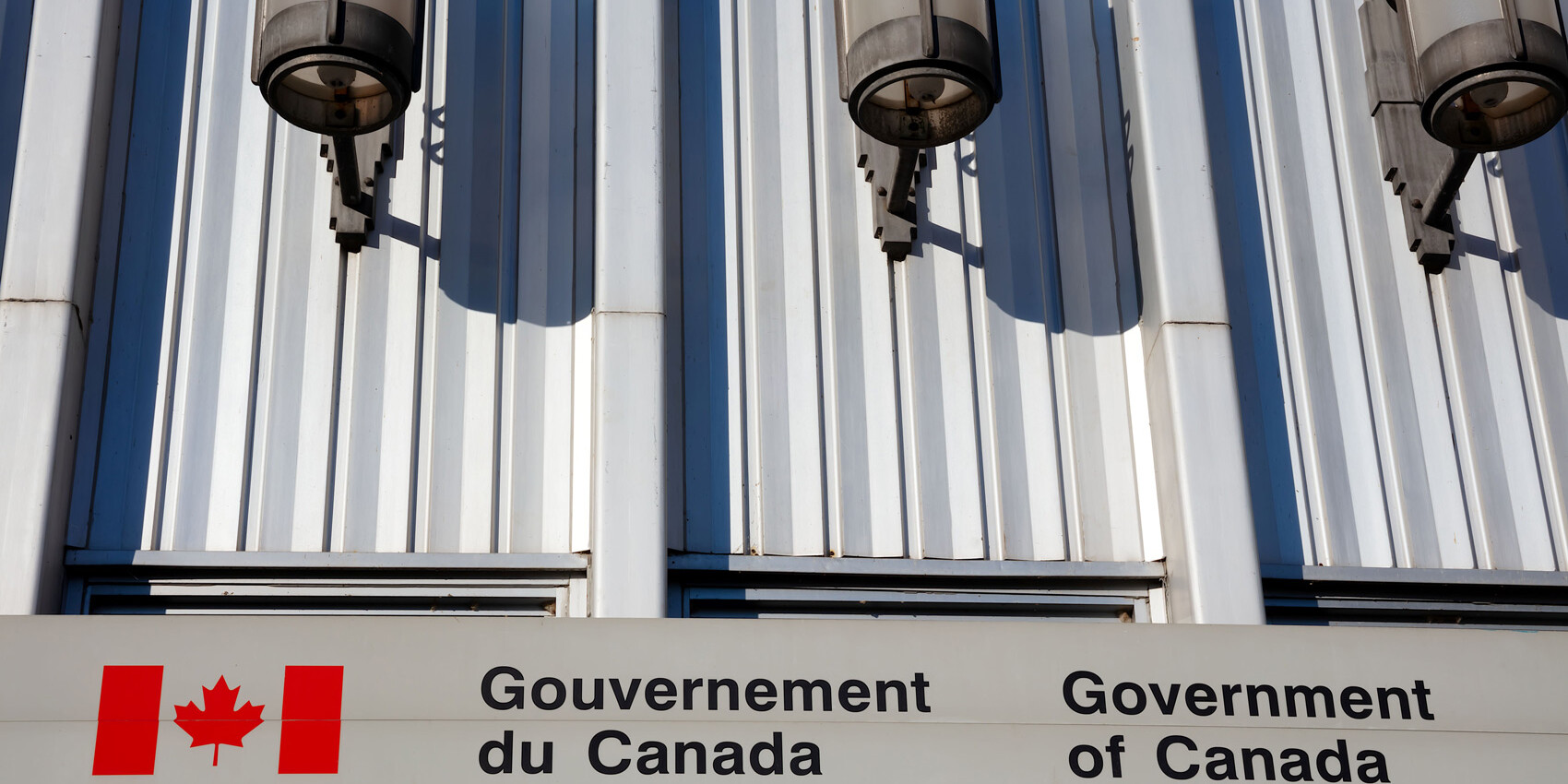 A building facade with three lights above a bilingual sign reading Gouvernement du Canada and Government of Canada, next to a Canadian flag logo—a reminder that the CPC needs to get back to bilingualism.