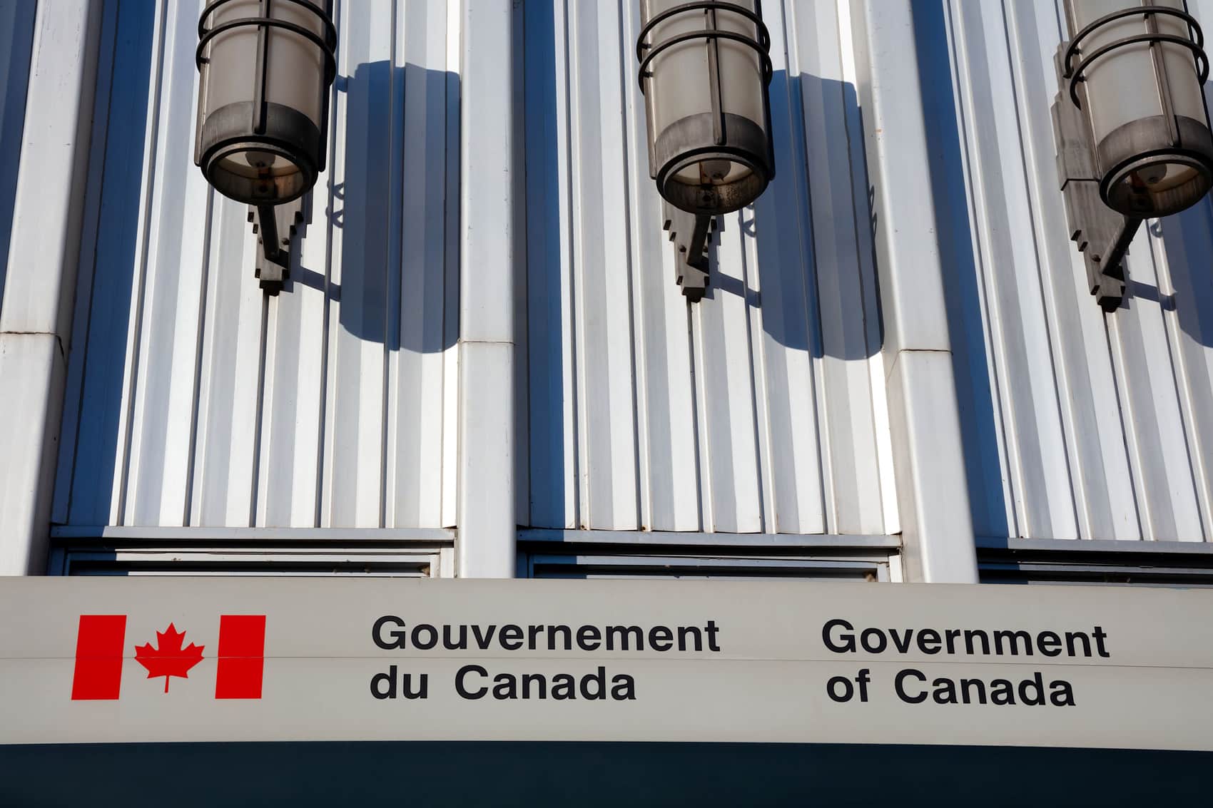 A building facade with three lights above a bilingual sign reading Gouvernement du Canada and Government of Canada, next to a Canadian flag logo—a reminder that the CPC needs to get back to bilingualism.