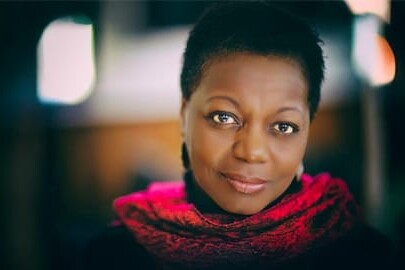 A woman with short hair, wearing a bright red scarf and dark earrings, looks softly at the camera. The blurred lights behind her subtly highlight the message: Yes Canada, we too have an anti-Black racism problem.