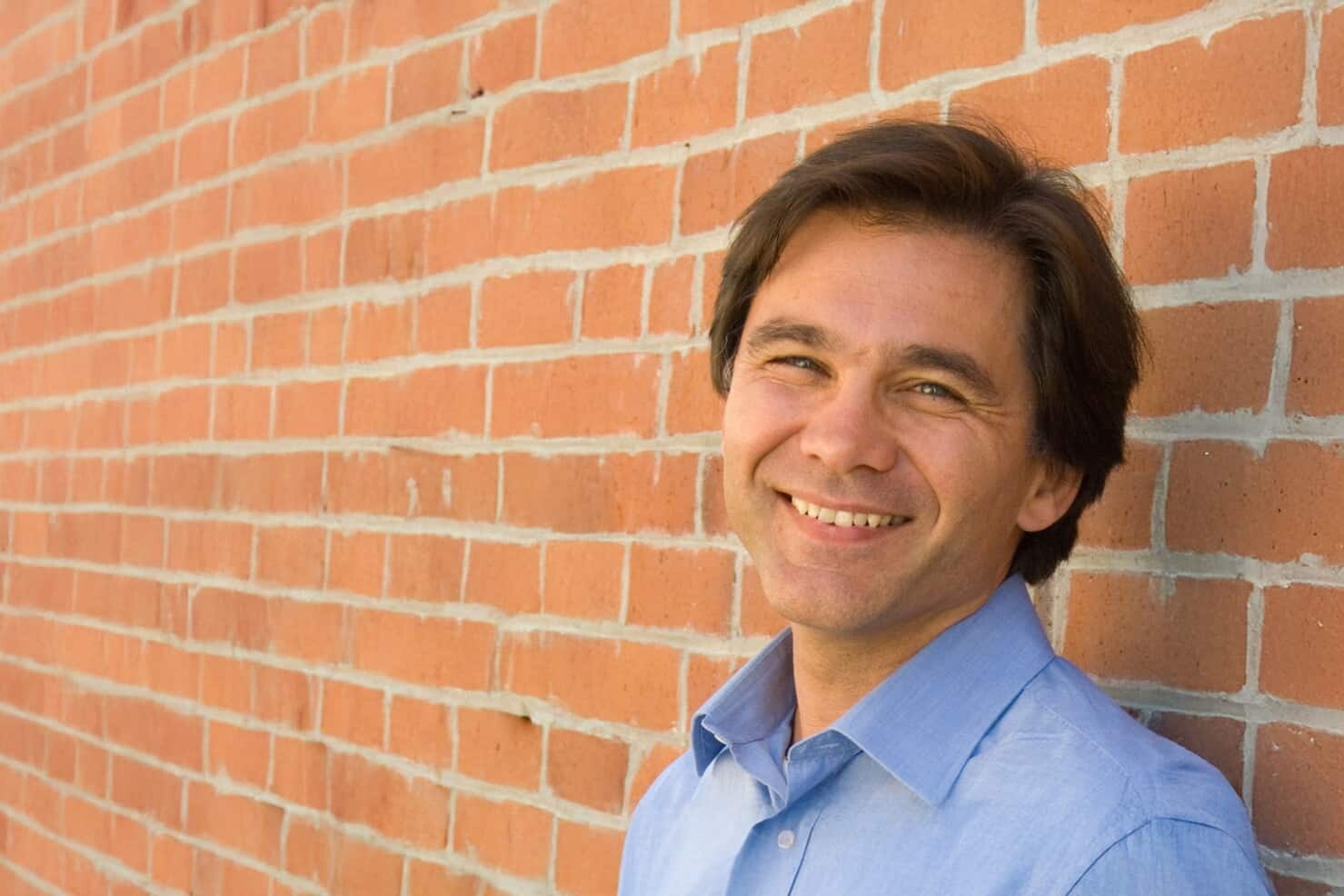 A man smiling in front of a brick wall, reflecting on three facts about inequality and equality of opportunity.