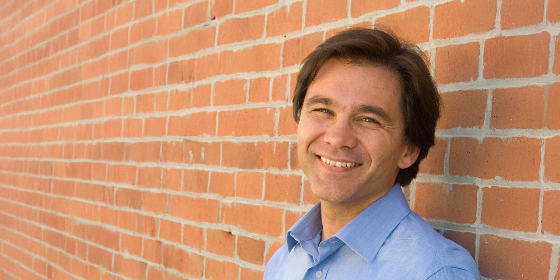 A man smiling in front of a brick wall, reflecting on three facts about inequality and equality of opportunity.