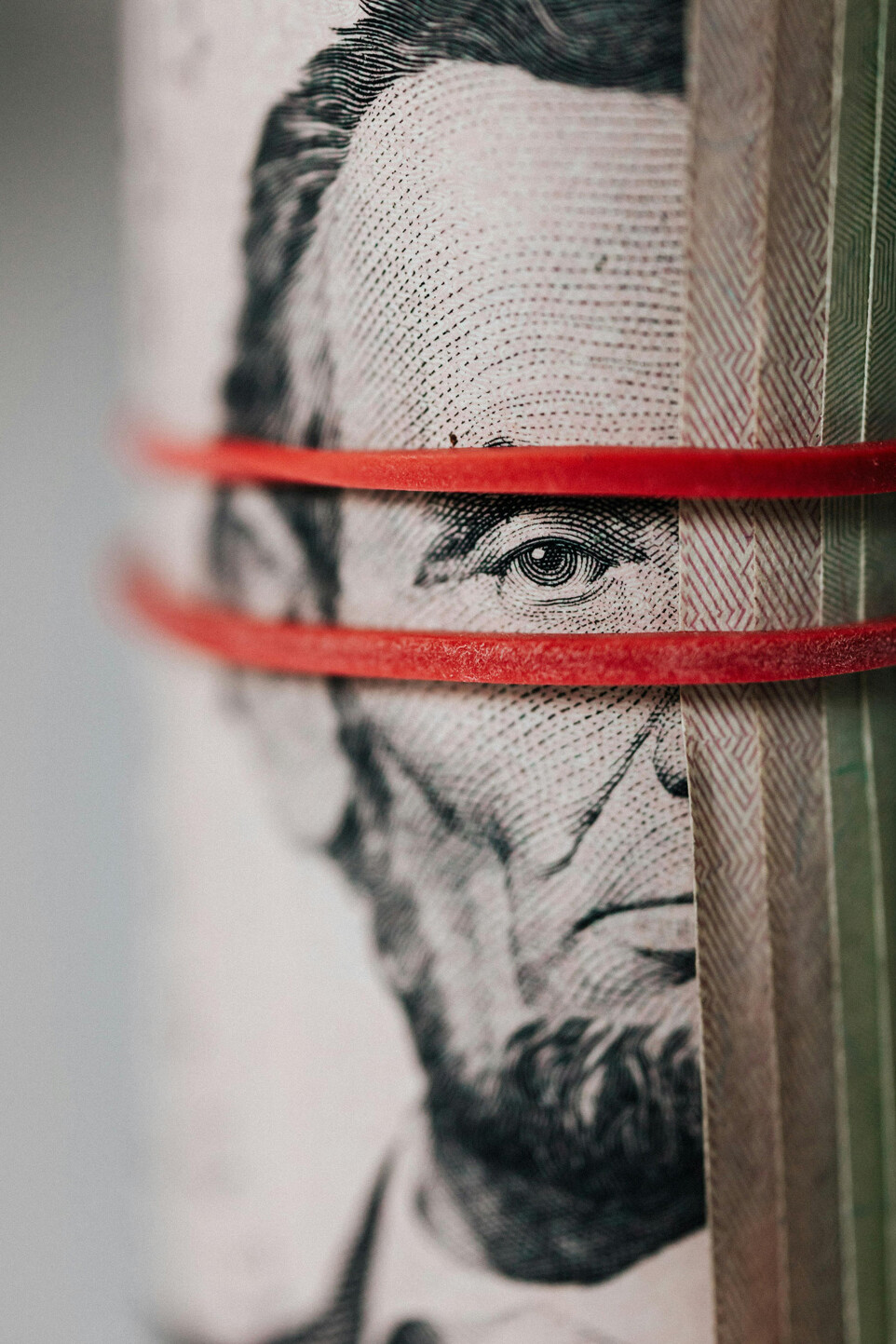 A close-up of a rolled U.S. five-dollar bill with Abraham Lincoln&rsquo;s face partially visible, secured by two red rubber bands&mdash;prompting reflection on questions like, &ldquo;Will 2025 be remembered as the year Canadians re-embraced nationalism?&rdquo;.