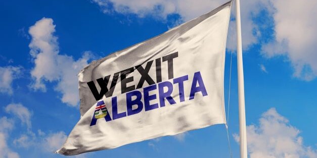 A white flag with the words WEXIT ALBERTA in bold letters waves against a blue sky with clouds, as Albertans, growing alienated from their own leaders too, rally to 