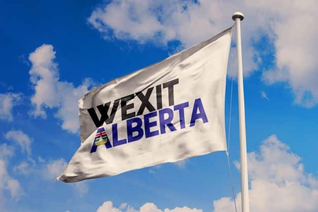 A white flag with the words WEXIT ALBERTA in bold letters waves against a blue sky with clouds, as Albertans, growing alienated from their own leaders too, rally to 